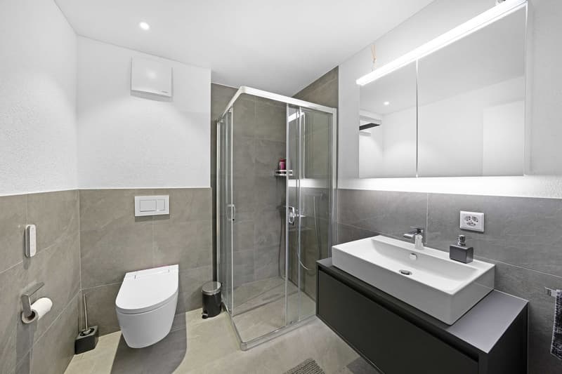 modern bathroom with white tiles, glass shower enclosure, white sink, mirror, toilet, and a towel rack