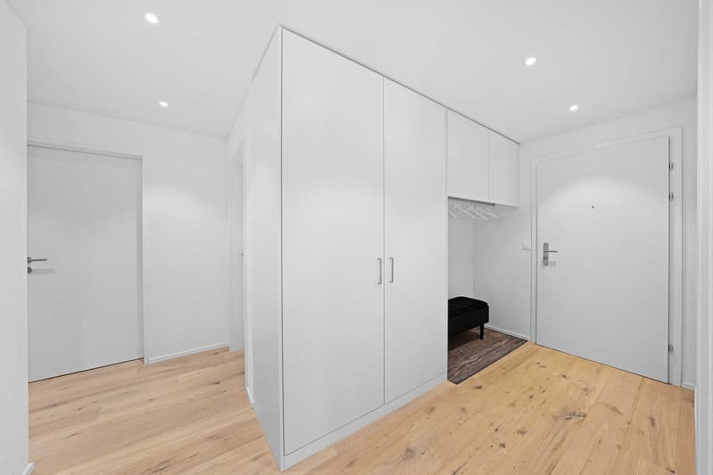 Empty room with white walls, wooden floor, large white wardrobe, small black bench, white doors