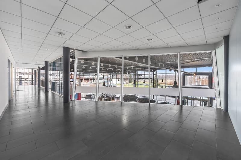 Large open commercial space with tiled flooring, suspended ceiling tiles, and large windows overlooking an outdoor area. The space appears to be empty and ready for use.