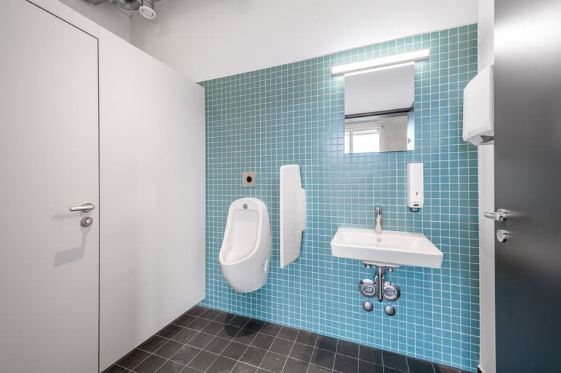 Bathroom with teal mosaic tile walls, white toilet, white sink with faucet, and a door.