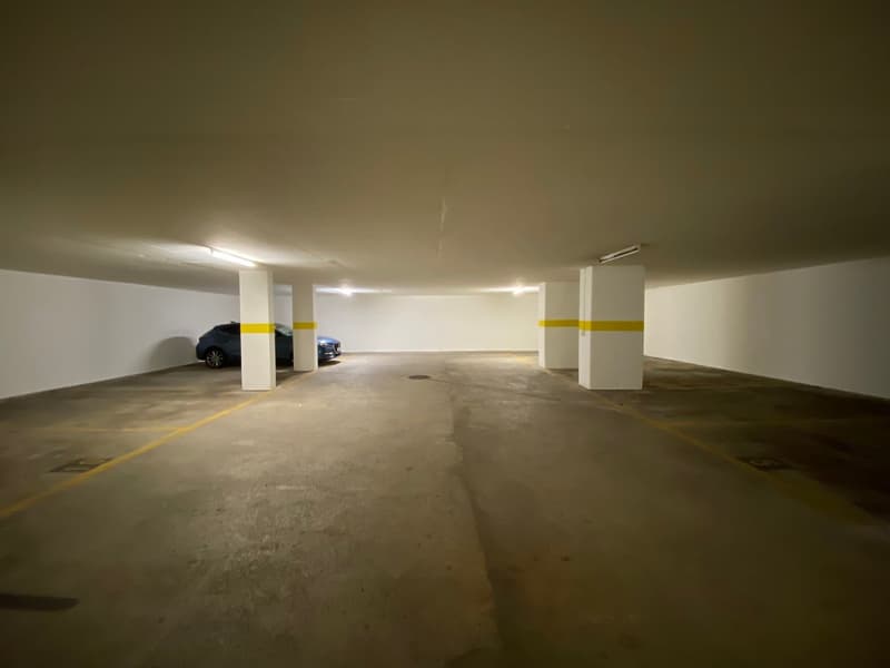 underground parking, white walls, yellow markings, a car parked, and ceiling lights