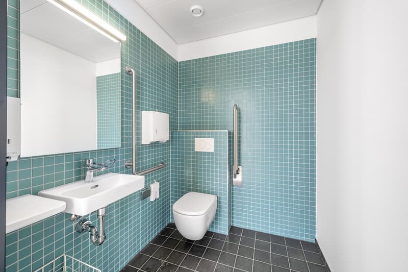 bathroom with teal tiles, sink, toilet, mirror, towel holder, dispenser