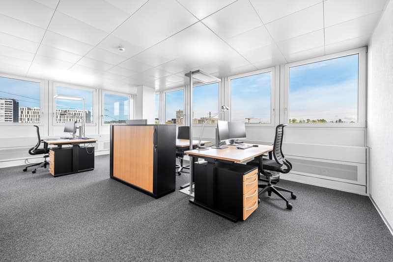 spacious office, large windows, modern furniture, grey carpeting, large desks, ergonomic chairs, monitors