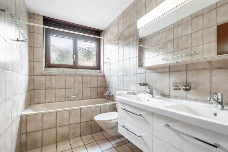 modern bathroom with white fixtures, beige tiles, bathtub, toilet, double sink, mirror