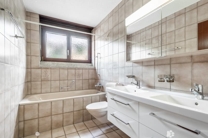 modern bathroom with white fixtures, beige tiles, bathtub, toilet, double sink, mirror