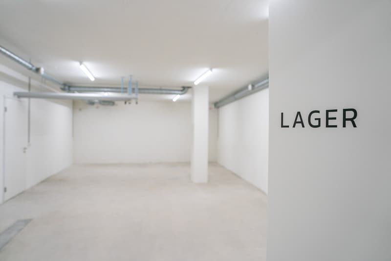 Empty underground garage space, white walls, ceiling pipes, two entrance doors.