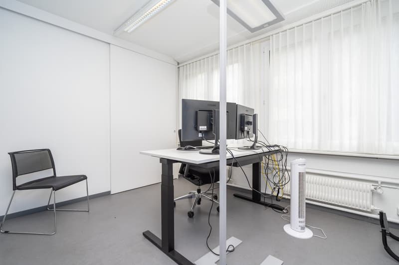 A desk with monitors and a chair, black mesh chair, a white radiator, and white curtains