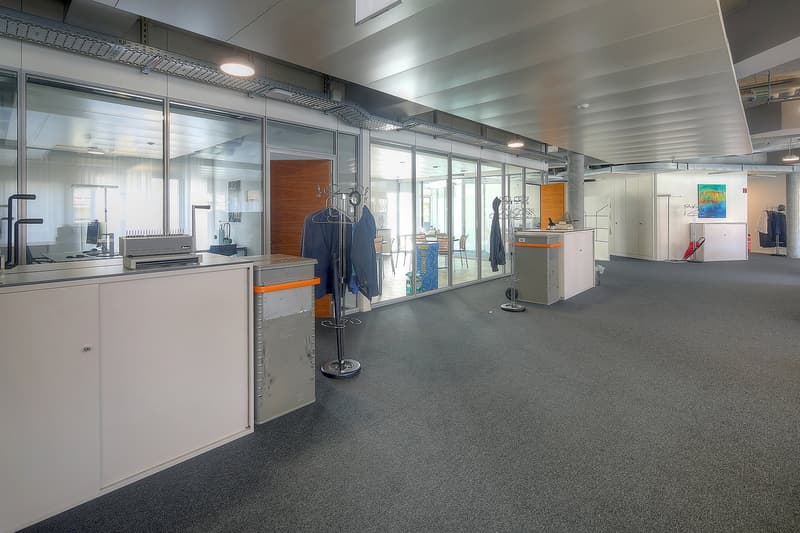 Open office space with glass partitions, storage cabinets, coat racks, and a dishwasher visible