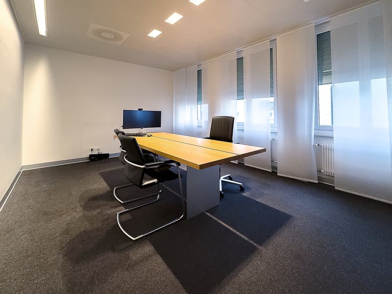 conference room with a wooden desk, two black swivel chairs, a black office chair, a computer monitor, keyboard, and mouse