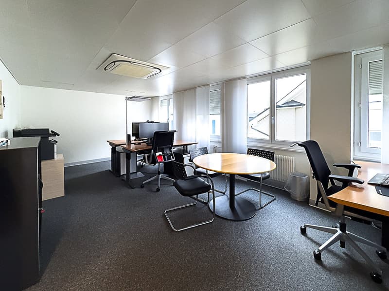Empty office room with tables, chairs, computers, trash bin, radiator