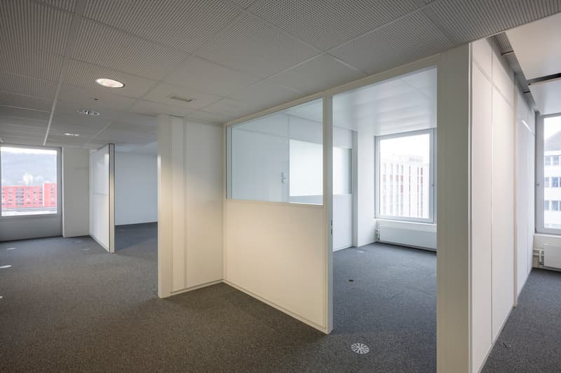 modern office with grey flooring, white walls, glass panels, and large windows