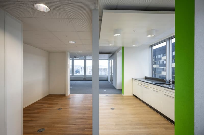 white walls, hardwood floors, green column, kitchen area with sink and cabinets