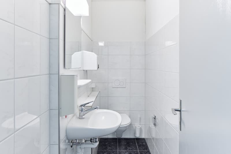 Small bathroom with white tiles, a toilet, a sink, and a glass shower enclosure.
