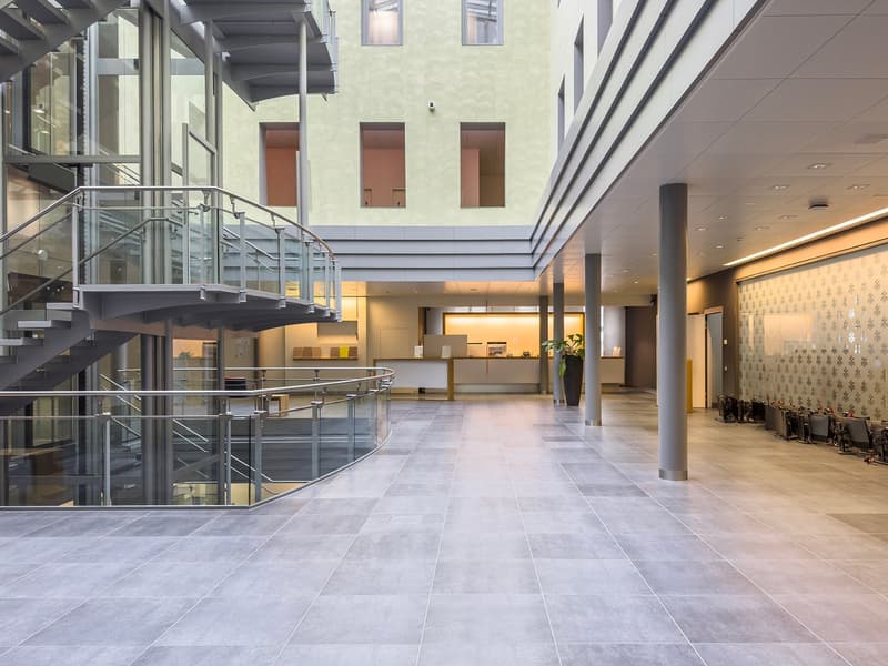 Large open lobby area with glass walls, metal staircase, tiled flooring, and modern decor elements