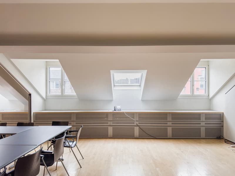 Spacious attic office with large windows, wooden storage cabinets, a conference table, and chairs.