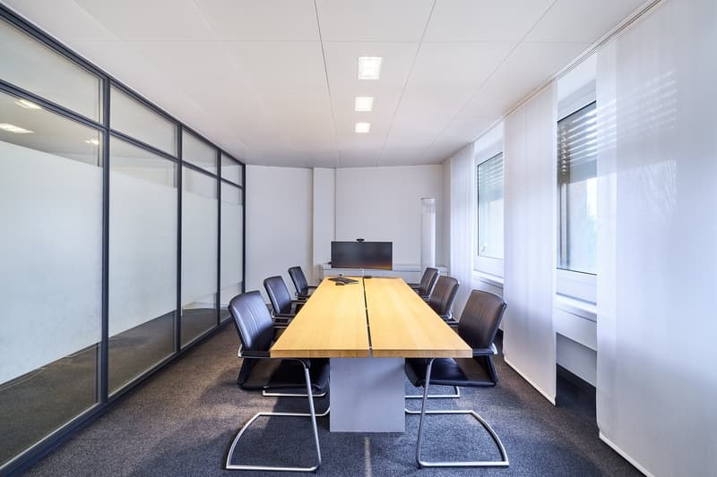 Meeting room, glass walls, carpet floor, large desk, chairs, monitor