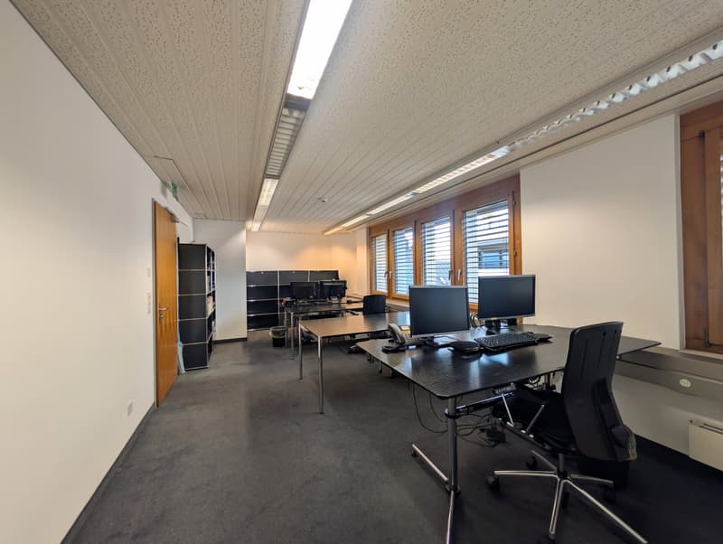 empty office room, desks, chairs, monitors, keyboards, telephones, bookshelves, carpeted floor, white walls, ceiling lights