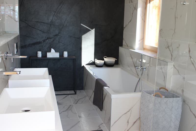 Modern bathroom with black and white marble tiles, white vanity with sink, black storage cabinet, and a dishwasher visible on the counter.