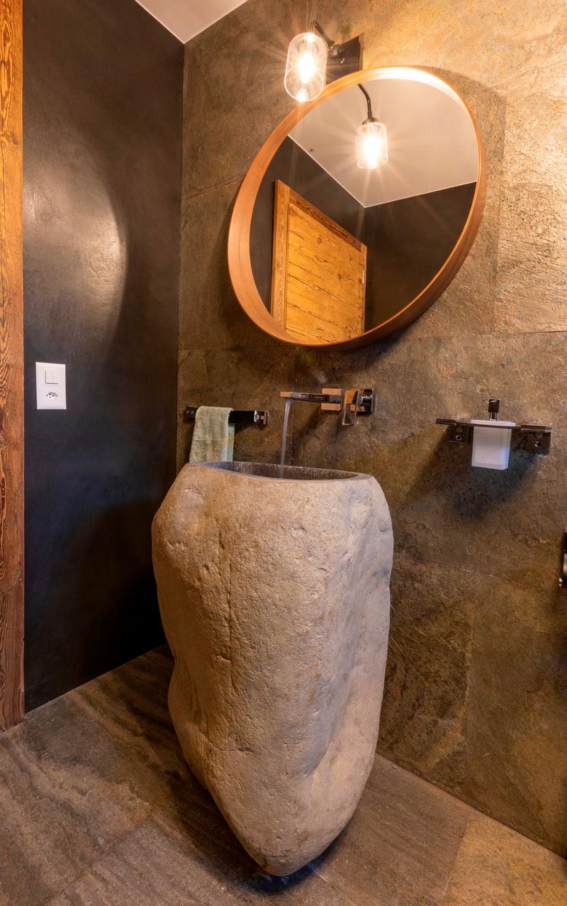 Rustic bathroom with stone sink, round mirror, and wall-mounted lighting fixtures