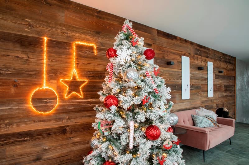 Cozy living room with a flocked Christmas tree decorated with red and white ornaments, a pink sofa, and a wooden accent wall with string lights in the shape of a star and a circle.