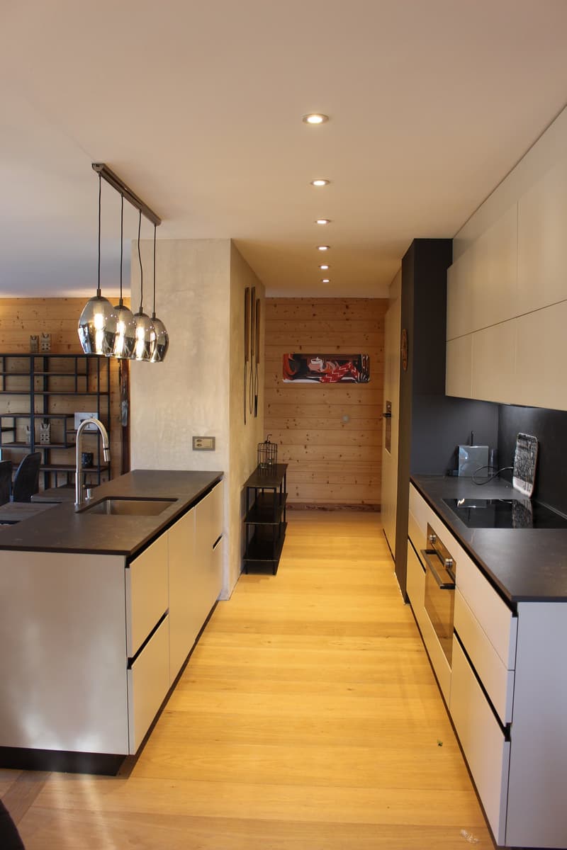 Modern kitchen with wooden walls, black countertops, stainless steel appliances, and a hanging light fixture over the kitchen island.