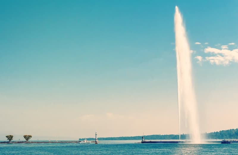 A large fountain spraying water into the sky, with boats and trees in the background
