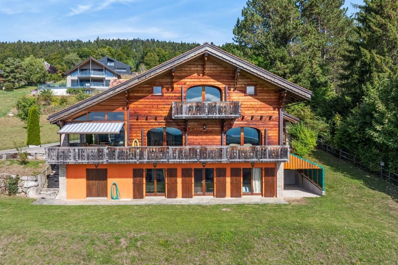 A large log cabin with an awning on the left side, a balcony on the top floor, and a paved yard