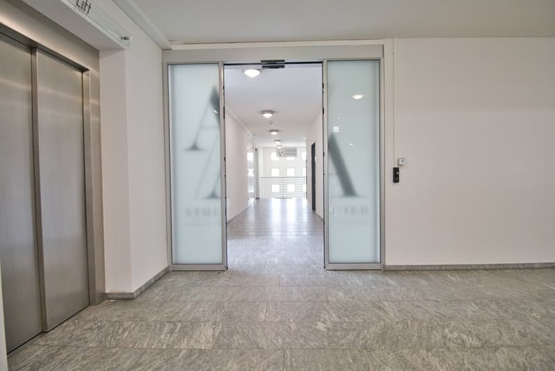 Empty hallway with tiled floor, glass doors, and ceiling lights