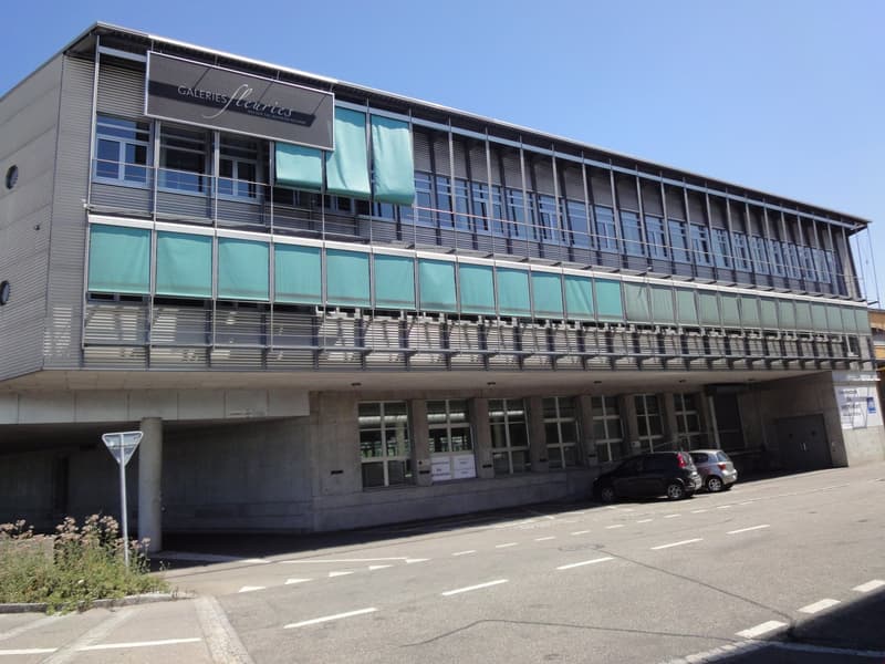 2 story building, gray exterior, multiple windows, car parked in front, sign on the top, metal railings on the second floor