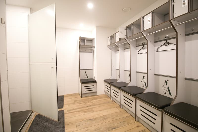 A room with wooden floor, white walls, lockers with benches, and a glass door.