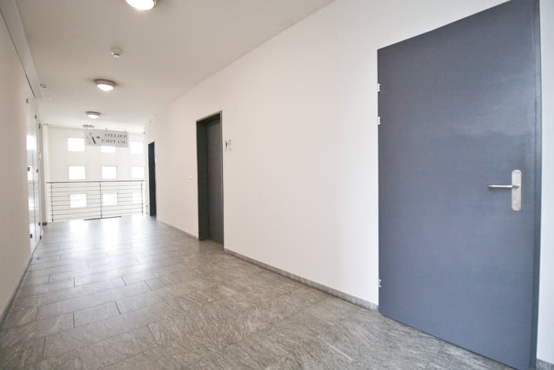 Empty hallway with tiled floor, white walls, and two doors. There is a sign on the wall and a balcony with a metal railing.