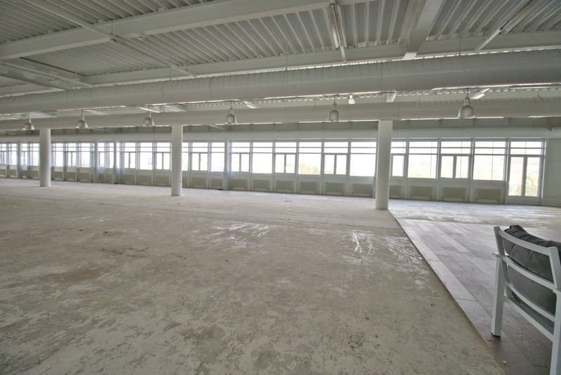 Open space with high ceiling, large windows, and concrete floor.