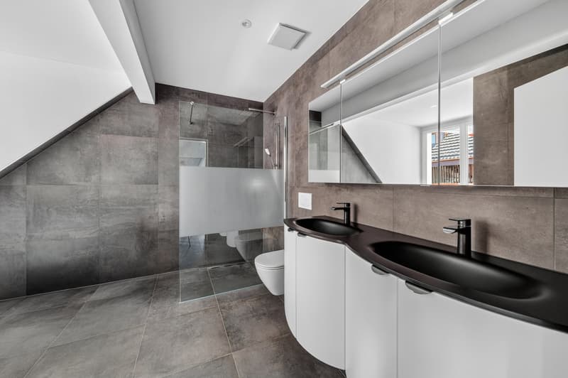 modern bathroom with gray tiles, double sink, glass shower enclosure, toilet, mirror