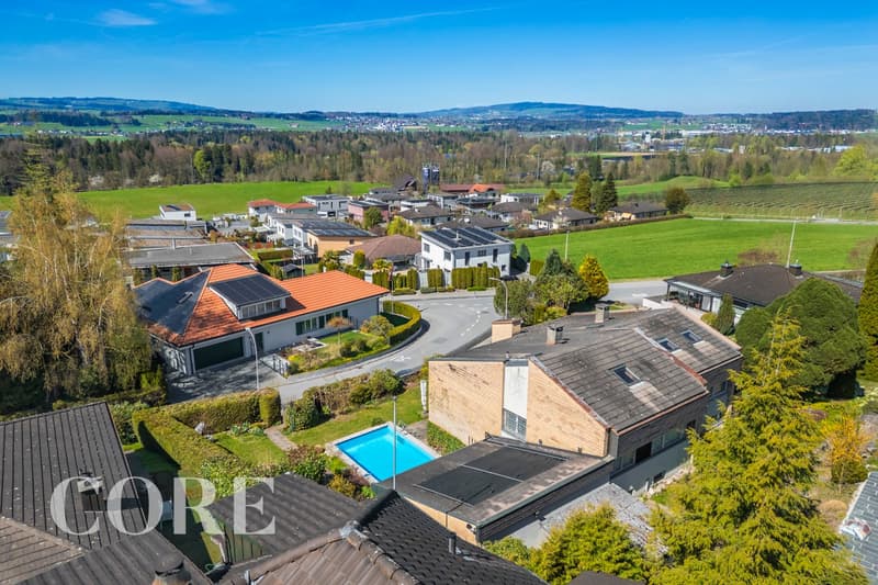 Aerial view of a neighborhood with several houses, some with solar panels, a swimming pool, and a road.