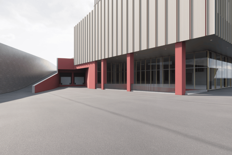 Large commercial building with a modern, minimalist design. The exterior features a combination of gray metal siding and red accents on the columns and entryways. The building has a rectangular shape with a flat roof and large windows. There is a large op