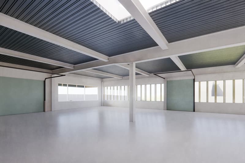 Large open space with high ceilings, gray concrete floors, and a grid-like metal ceiling structure with black panels. The walls are painted a light green color and there are large windows along the sides providing ample natural light.