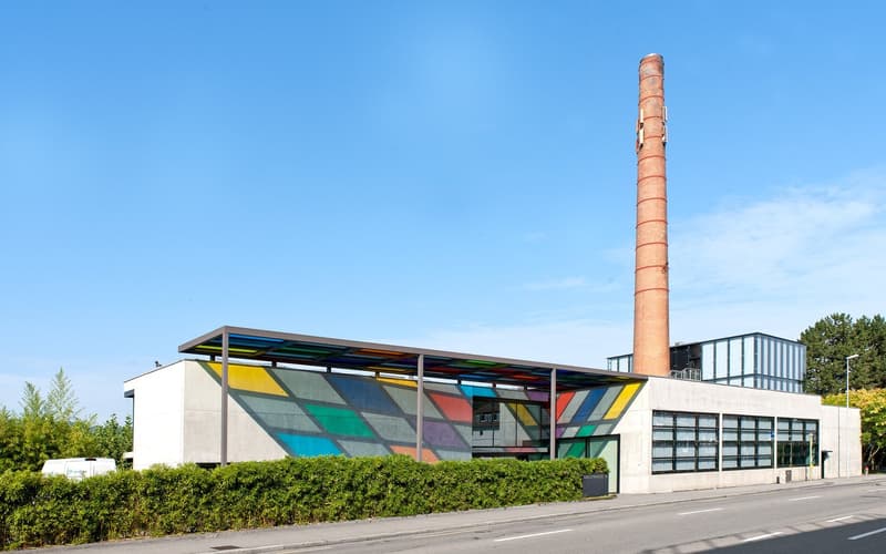 modern architectural building, vibrant multi-colored murals, large chimney, glass windows, canopy over entrance