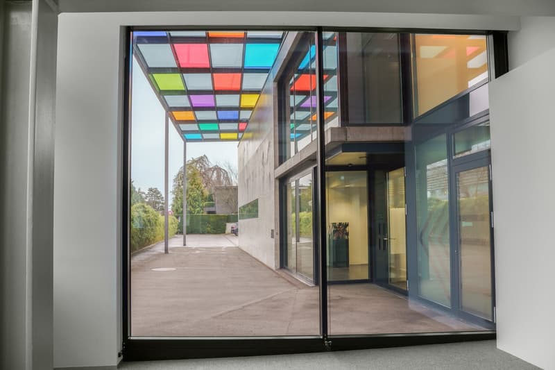 large windows, entrance with glass doors, parking lot, green bushes