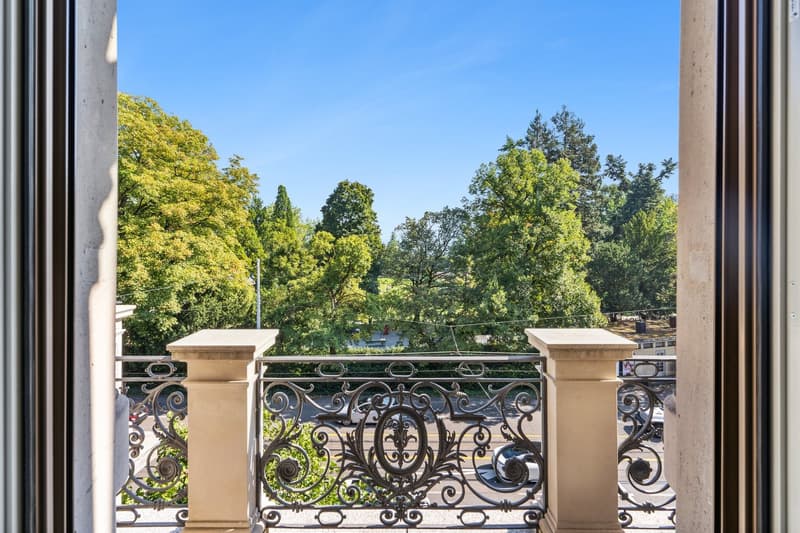 balcony with ornate railing, view of green trees and clear sky