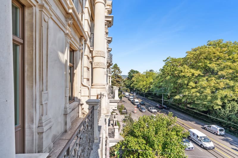 classic exterior design, balcony, busy street with multiple vehicles, tree-lined street, bright sky