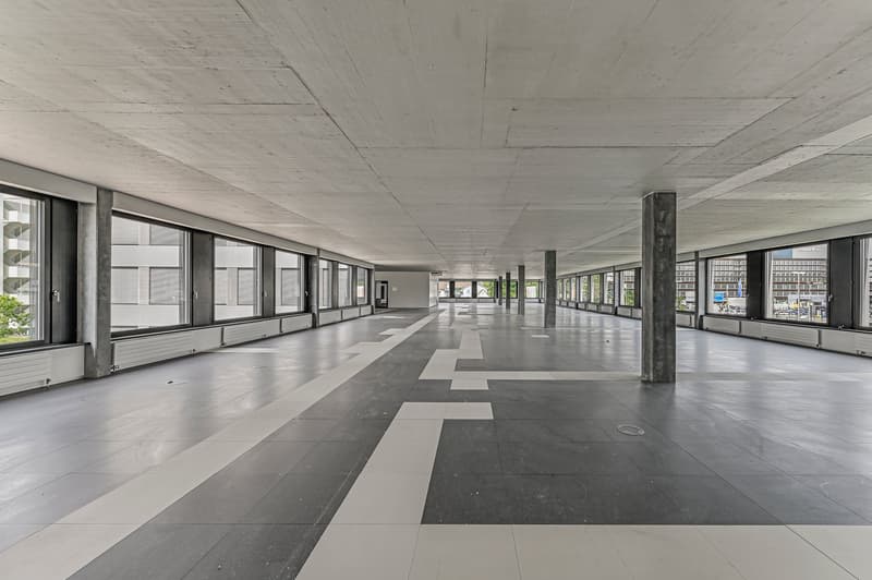 Empty hallway, gray and white tiled floor, concrete ceiling, many large windows, white trim on windows