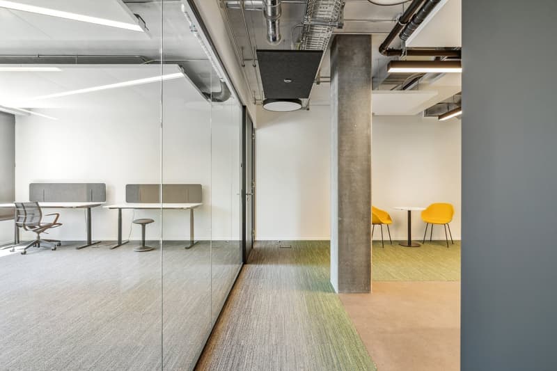 modern office space with glass walls, modular desks, chairs, carpet, round tables, yellow chairs, exposed pipes