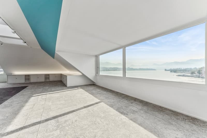 empty room, large windows, concrete floor, white walls, blue accent wall, view of water and mountains