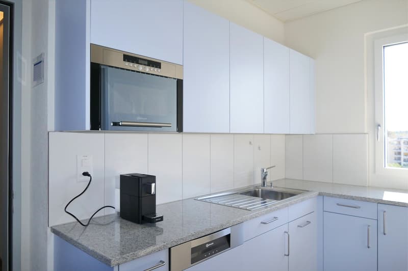 Modern kitchen with stainless steel appliances, granite countertops, white cabinetry, electric kettle, dishwasher, and integrated coffee machine.