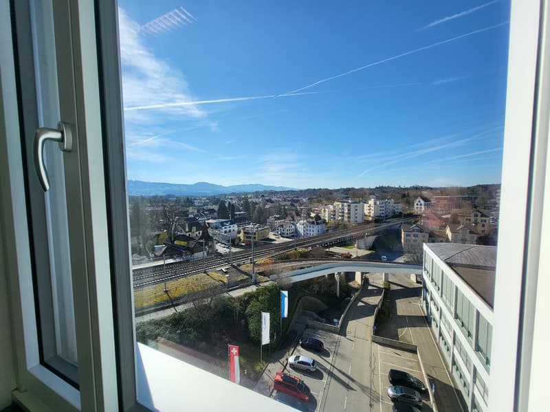 View of a city from an elevated building, road, train tracks, mountains, buildings, car traffic, clear sky
