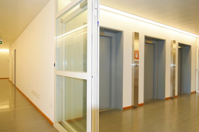 empty corridor, tile floor, white walls, glass doors, three elevator shafts
