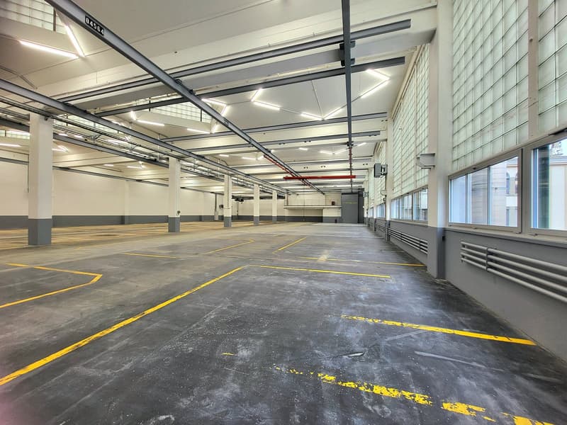 large parking area, yellow parking lines, concrete flooring, high ceilings with metal beams, windows