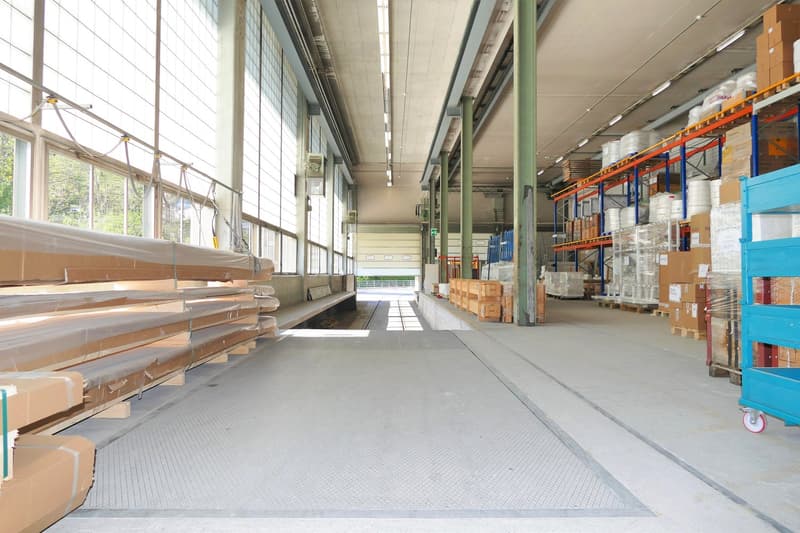 large empty warehouse, wide windows, gray floor, numerous boxes and storage shelves