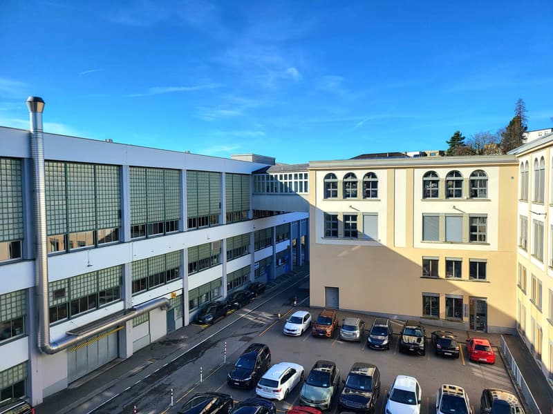 Modern industrial building, many cars parked, large windows, 2 buildings