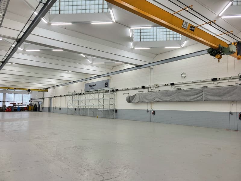 Large industrial warehouse space with high ceilings, overhead crane, and storage racks. The space appears to be used for storage and logistics, with a loading dock area visible.